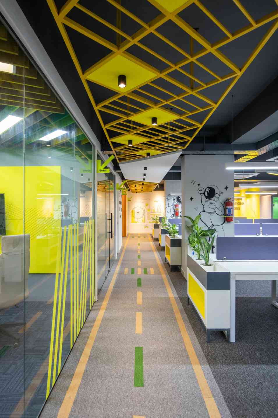 hallway with glass wall, cubicles, plants, multicolored carpet, patterned ceiling