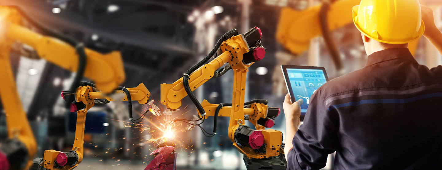 Back of man operating screen and two yellow machinery arms working on item, sparks flying off of it