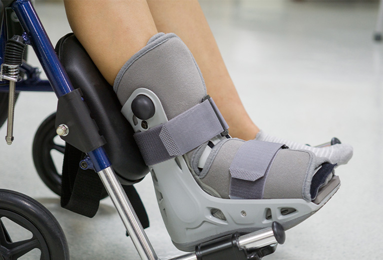 legs of person in a wheelchair, one foot with a detachable cast/boot